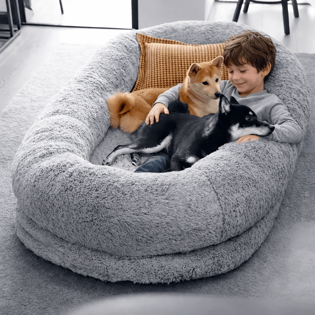 Enfant allongé avec deux chiens dans un panier pour chien moelleux et confortable, idéal pour le repos et les moments de détente à la maison.